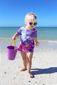 一个可爱的2岁蹒跚学步的小女孩正在海边的沙滩上玩耍图片