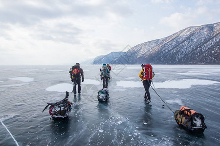 背着包穿冰水表面和背景山丘的三人图片