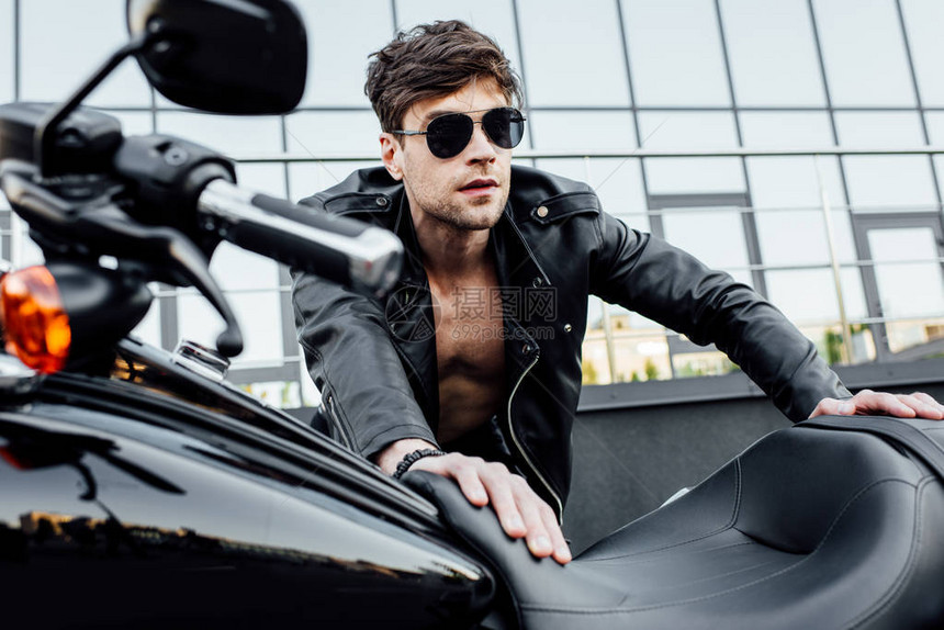 在太阳镜和黑皮夹克中专挑帅男的焦点仰着摩托车图片