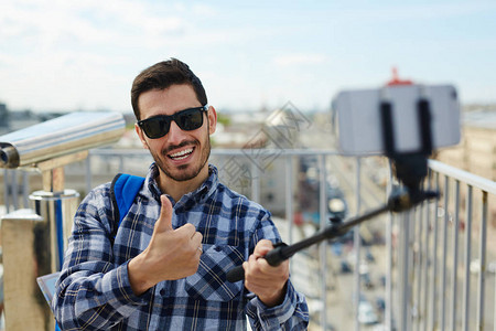 英俊年轻男子站在屋顶上对着相机竖起大拇指自拍照片图片