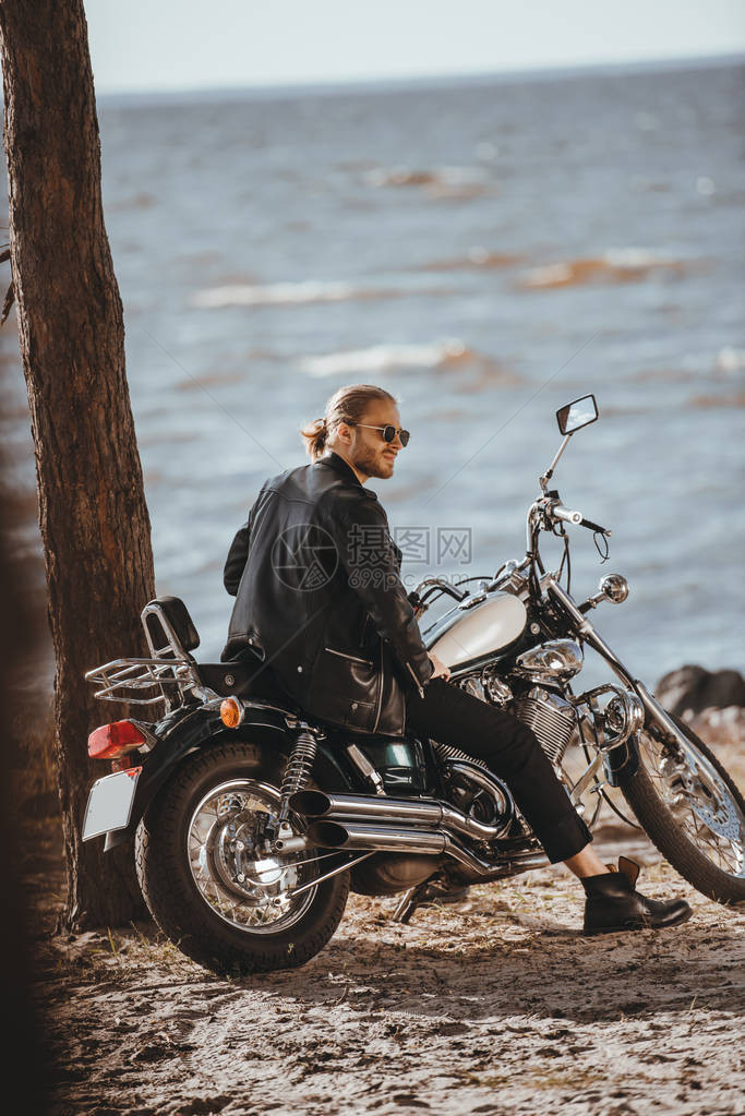 穿着黑色皮夹克的摩托车坐在海上附近的古典直图片