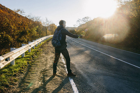 在乡间小路上搭便车的人旅行者在公路旅行期间为搭便车而竖起大拇指冒图片