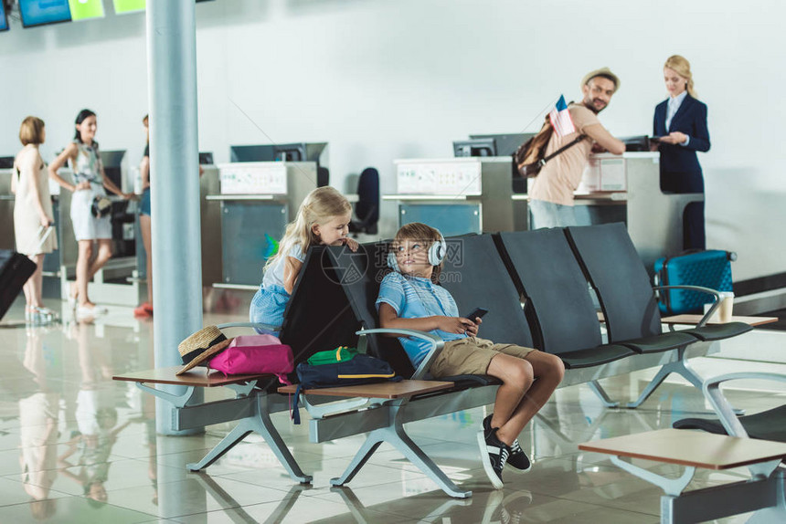 戴耳机的男孩与附近的妹和父亲在机场的登机柜台图片