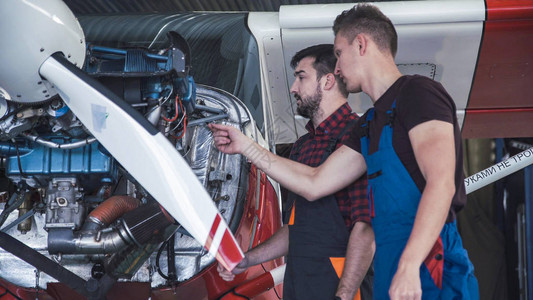 两名机械师在一个机库内的小飞机上工作图片