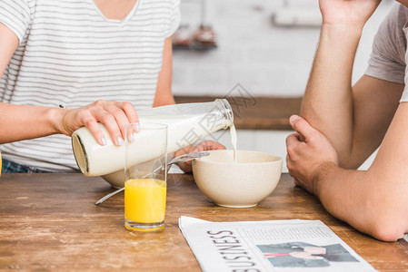 在厨房早餐时将奶水从瓶中倒到盘子里的玉米片图片