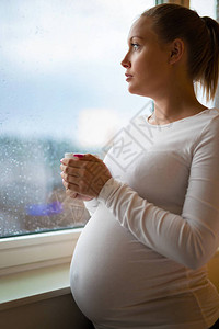 怀有想象力的怀孕妇女看着窗外的家图片