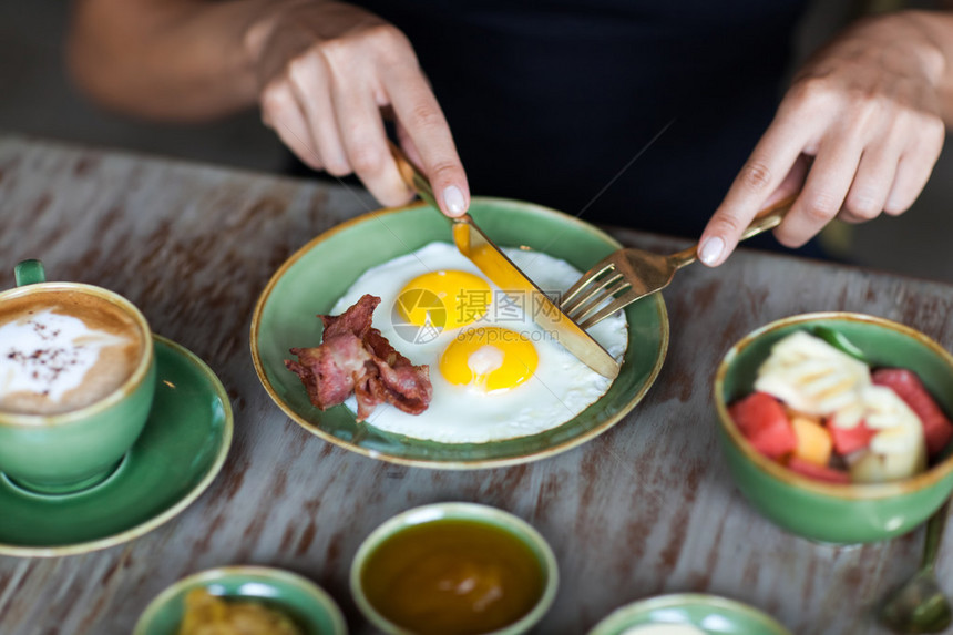早餐时用金叉和刀切煎鸡蛋的女人图片