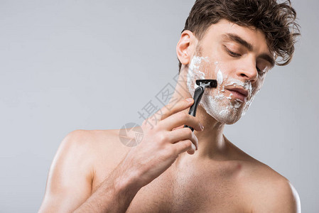 长相英俊的caucasian男子泡沫在脸部刮剃须刀图片