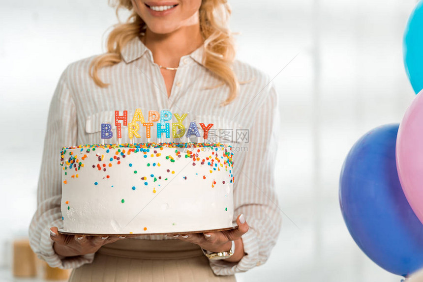 带着彩色蜡烛和生日快乐信的生日蛋糕与微笑的妇女所看到的景象图片