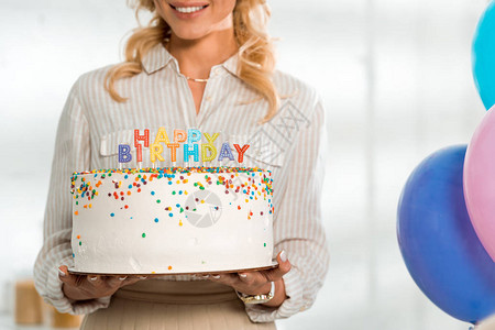 带着彩色蜡烛和生日快乐信的生日蛋糕与微笑的妇女所看到的景象图片