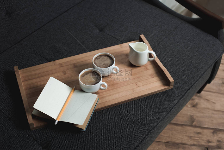 两杯咖啡一壶牛奶和笔记本在沙发上的图片
