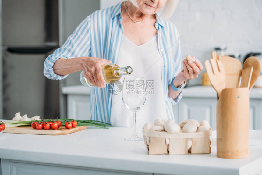 在柜台上用厨房新鲜蔬菜把葡萄酒倒入杯子的高级妇女图片