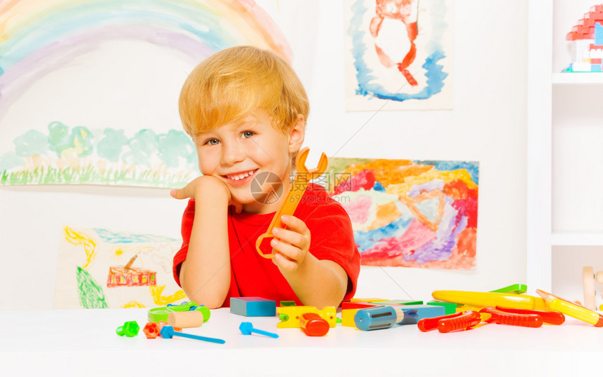 在幼儿园上课时坐在桌边坐着的拿着塑料玩具扳手的金发图片