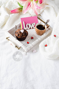 床上的木盘上配有巧克力和黑咖啡的松饼或奶粉图片