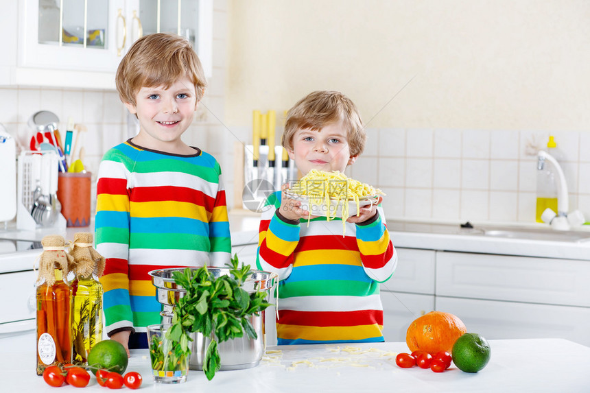 两个可爱的小男孩用意大利面和新鲜蔬菜在室内家用厨房做饭和吃饭图片