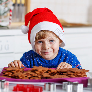 穿着红圣塔帽的可爱小男孩配着新鲜烤姜饼干祝大家对姜饼男人快乐图片