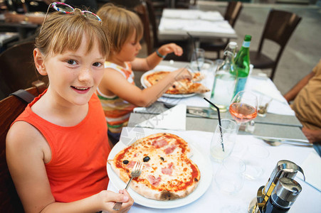 快乐的小女孩在餐厅里吃小孩的比萨饼图片