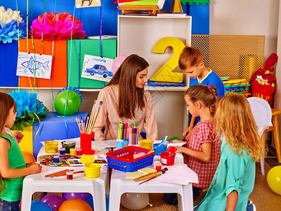 孩子们在幼儿园的桌子上和老师的女人在纸上画有老师的孩图片