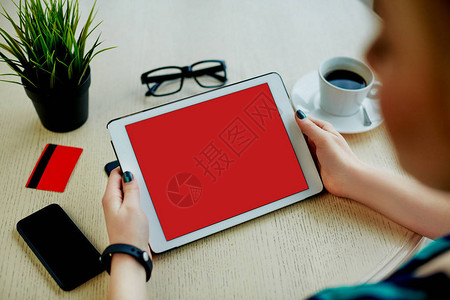 女人的手上拿着红色的平板电脑信用卡眼镜手机和桌上的咖图片