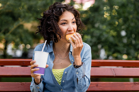 年轻女子享受快餐鸡汉堡和苏打水在图片