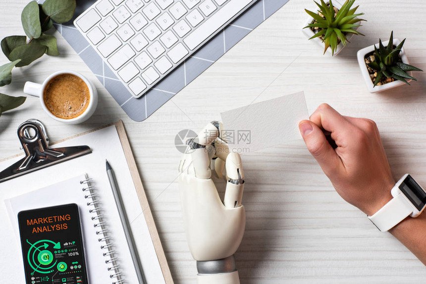 部分视图的商人用机器人手和智能手表在桌子上拿着空白访问卡图片