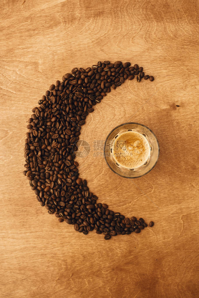 热浓咖啡与玻璃杯中的泡沫和木桌上月亮形状的芳香烤咖啡豆图片