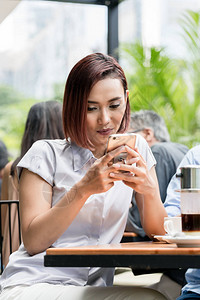 一名年轻亚洲女在咖啡店使用手机与网外户露天连线图片