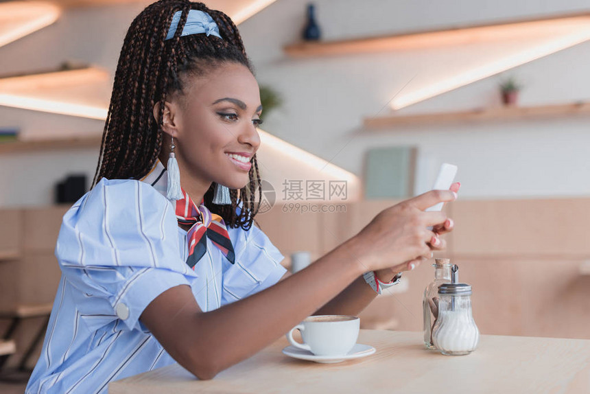 在咖啡店的智能手机上打字的年轻非裔美国女人每天图片