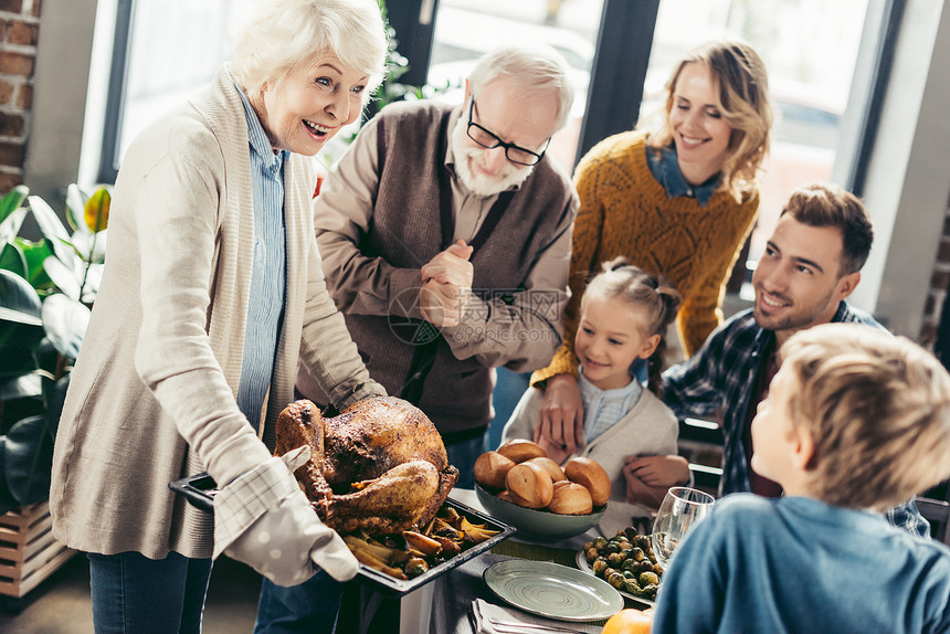感恩节晚餐时微笑的祖母为家人端着火鸡图片