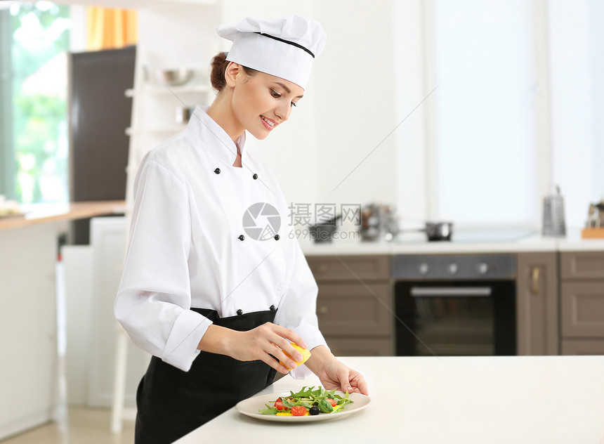 年轻女厨师在厨房里用柠檬汁调味沙拉图片
