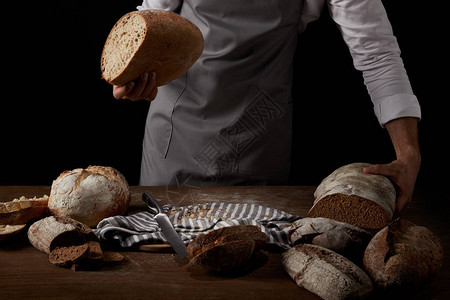 围裙男面包师用刀面包和麻布把面包放在桌子图片
