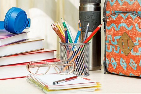 书本金属标牌和彩色铅笔热水器眼镜钢笔和木制桌上的笔记本图片