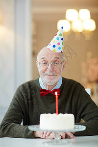 戴着生日帽的老人在蛋糕前坐在桌图片