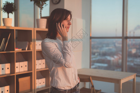 晚上在办公室用手机说话的年轻妇女图片