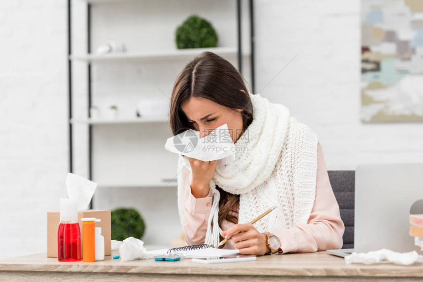 在工作场所用纸巾打喷嚏的年轻患病女图片