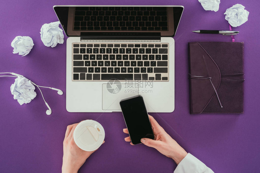 女商人使用智能手机和在工作场所用紫色表面喝咖啡的实干镜图片