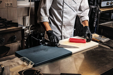 身穿制服的厨师和在厨房切割板上准备寿司的手图片