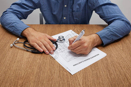 持有听诊器和在木制桌子上签署保险表背景图片