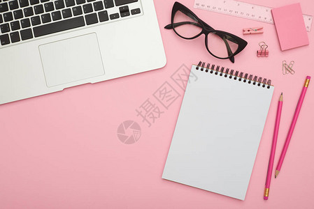 粉色桌上有银笔记本电脑眼镜和文具背景图片