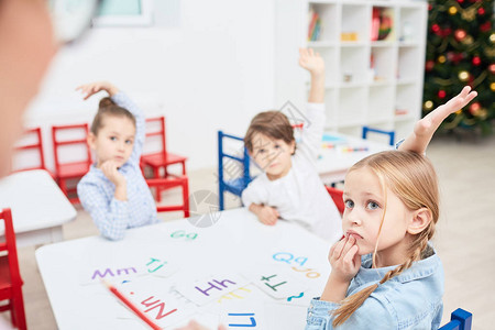 三个举起双手的小孩坐在桌旁在幼儿园的图片