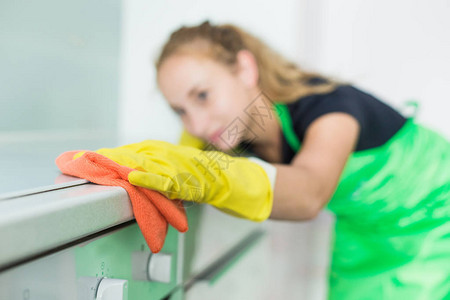 女手在橡胶黄色手套清洁家用厨房炊具面板的特写镜头图片