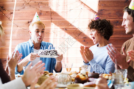 欢庆的朋友们祝贺年轻人在生日蛋糕上吹蜡图片