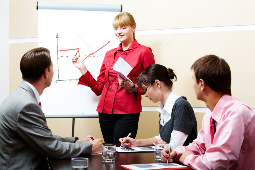 一位聪明的女在研讨会上的白板上指着白板而商业伙伴图片