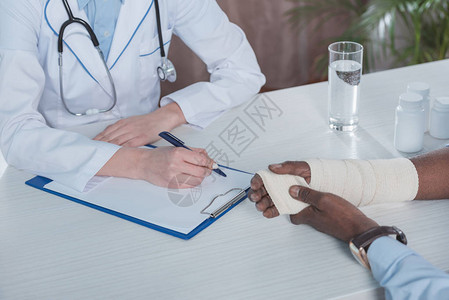 与手受伤的非裔美国病人坐在桌旁的医生图片