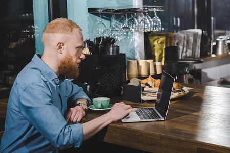 在咖啡店用带空白屏幕的笔记本电脑拍摄英俊胡子青图片
