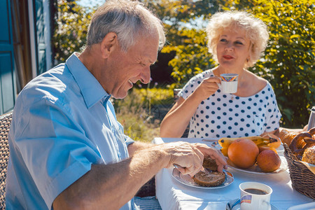 老年妇女和男子夏天在花园户外露天吃早餐吃面包卷和喝咖啡的年图片