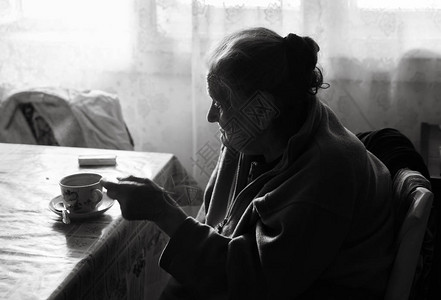 一位抑郁的老妇人的黑白图像一位孤独的老年妇女坐在靠近窗户的厨房的一背景图片