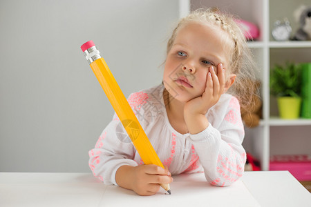 小女孩一边用大铅笔写字一边思考图片