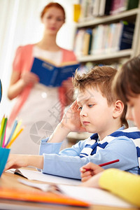 一个小男孩坐在桌边学习老师站在后背图片