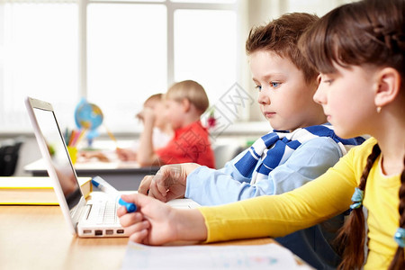 两个小孩子坐在学校的桌子上看笔图片
